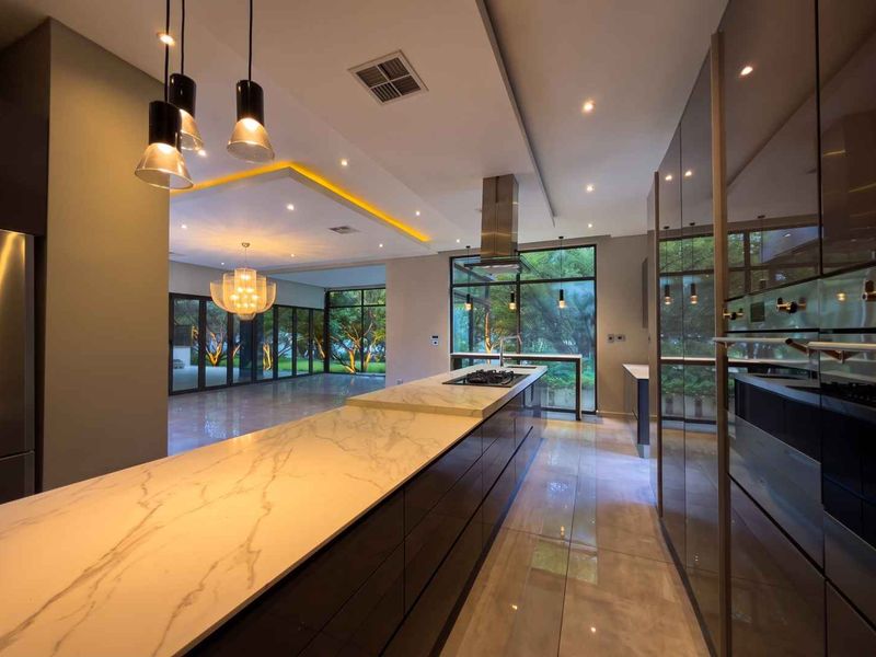 Modern open-plan kitchen and living area featuring a large marble island, high-end built-in appliances, recessed lighting, and expansive glass doors overlooking the garden.