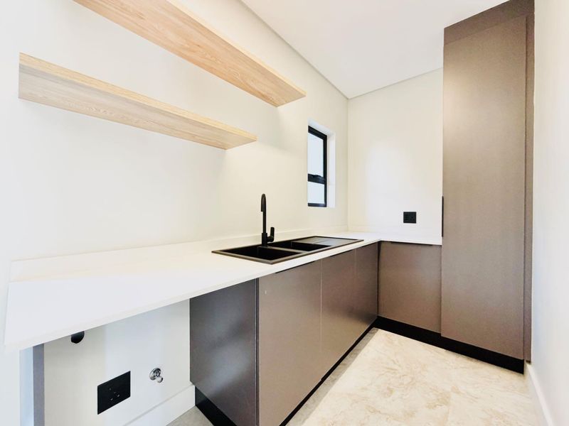 Modern scullery featuring sleek cabinetry, stone countertops, a double sink with black fixtures, and floating timber shelving.