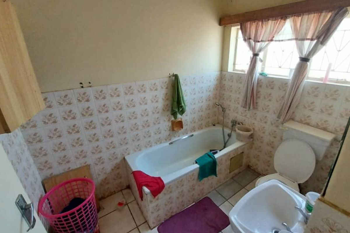 A dated bathroom featuring a standard bathtub, toilet, and basin with tiled walls and flooring, requiring modernization and cosmetic updates.