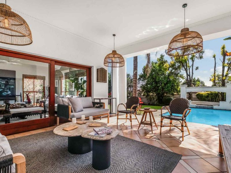 A spacious covered patio featuring tiled flooring and large sliding glass doors, overlooking a private swimming pool and landscaped garden area.