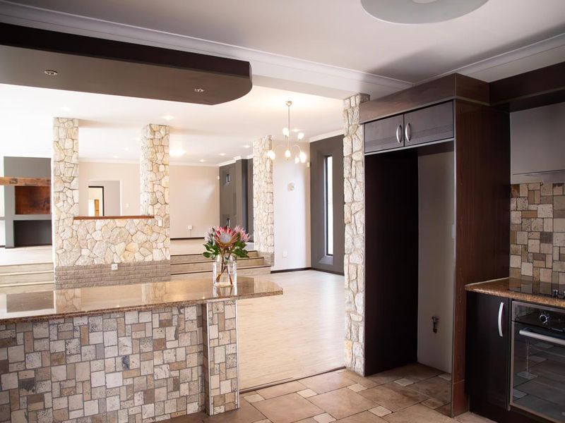 Spacious open-plan living and kitchen area featuring stone-clad pillars, granite countertops, and modern built-in cabinetry with integrated oven and hob.