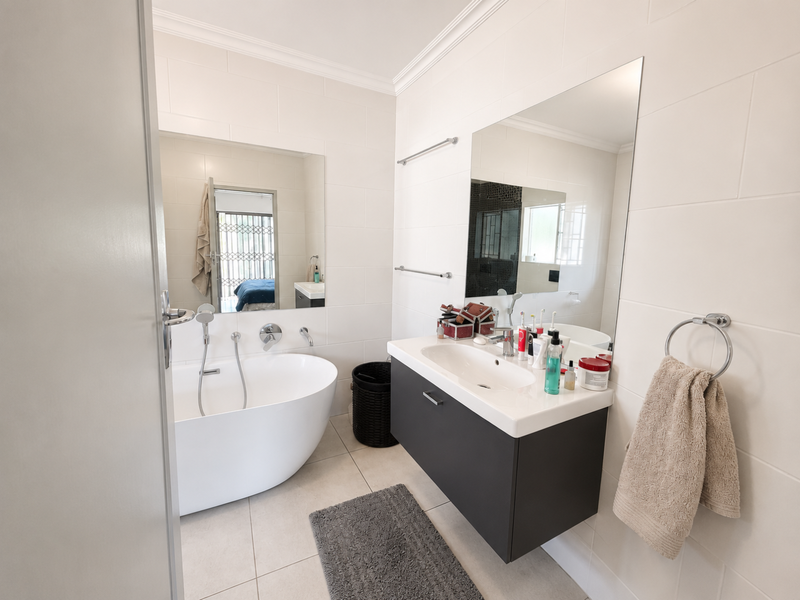 Modern bathroom featuring a sleek freestanding bathtub, a wall-mounted vanity with basin, and large mirrors, finished with clean white wall tiling.