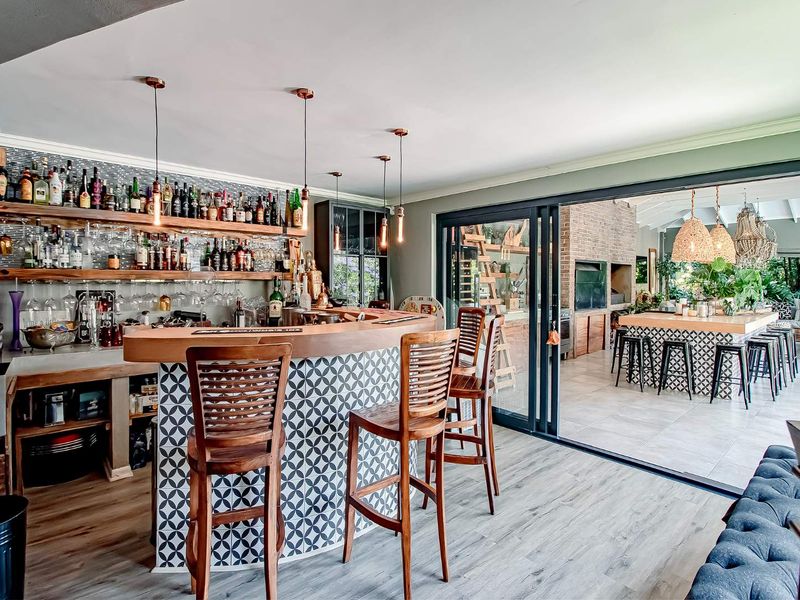 A stylish indoor bar area featuring custom cabinetry, patterned tiling, and open shelving, seamlessly connected to an outdoor patio entertainment space through sliding glass doors.