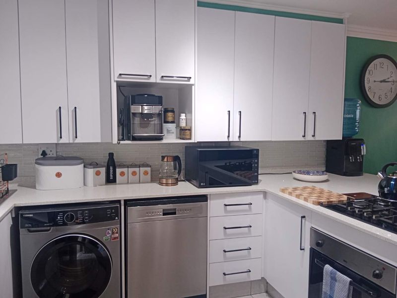 A modern kitchen featuring white cabinetry, stone countertops, a tiled backsplash, and integrated appliances including an oven, hob, dishwasher, and washing machine.