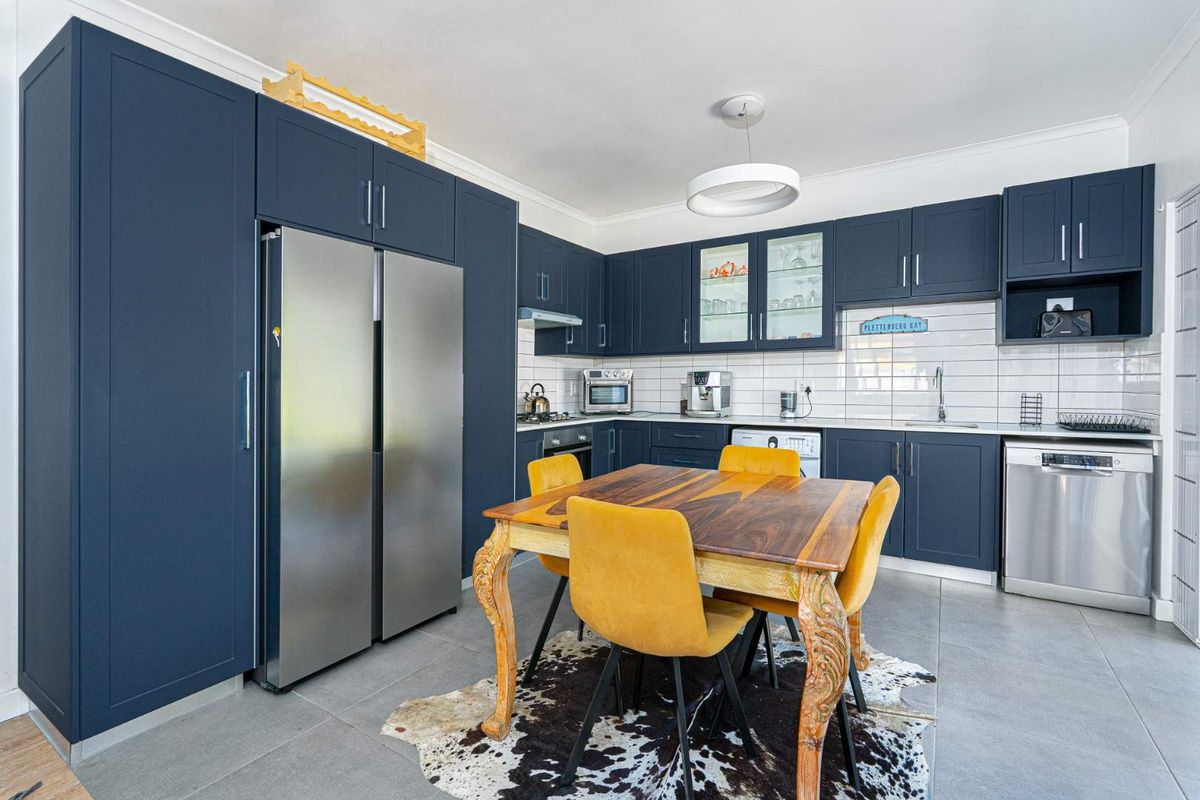 Modern kitchen featuring dark blue cabinetry, subway tile backsplash, integrated appliances, and a dedicated dining area with tiled flooring.