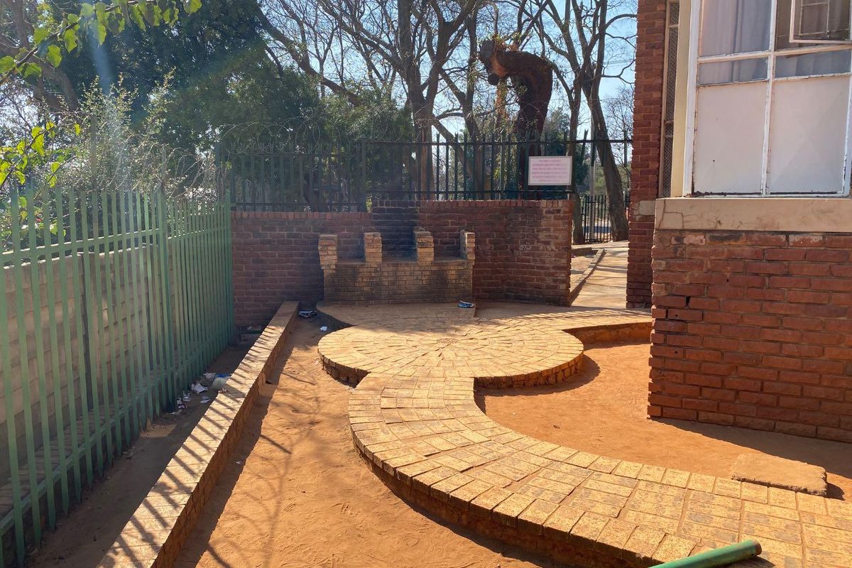 Rear outdoor area featuring brick paving, a built-in brick seating structure, and perimeter security fencing.