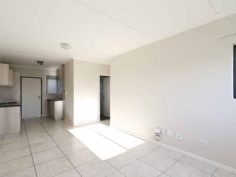An open-plan living and kitchen area featuring neutral tiled flooring, built-in cabinetry, and integrated kitchen appliances in a clean, vacant space.