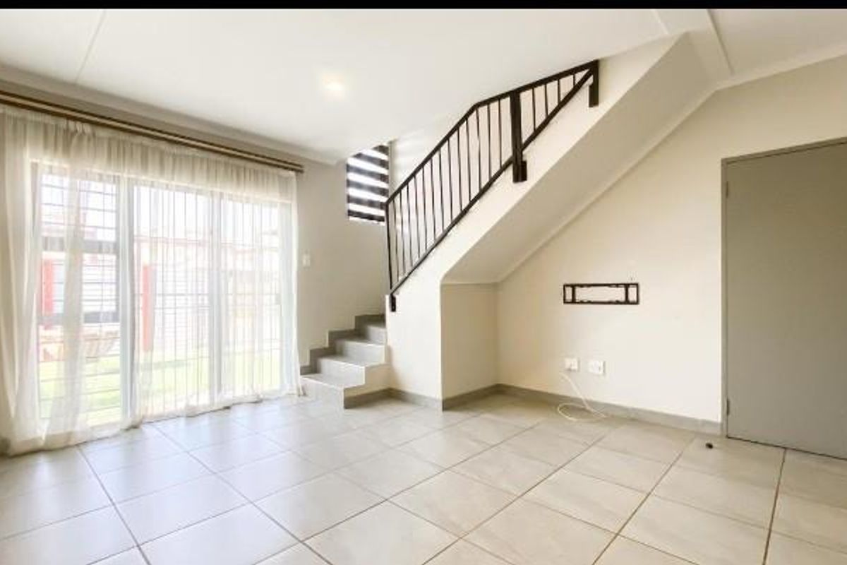 A bright, open-plan living area featuring tiled flooring, a staircase with a metal balustrade, and large sliding glass doors leading to the exterior.