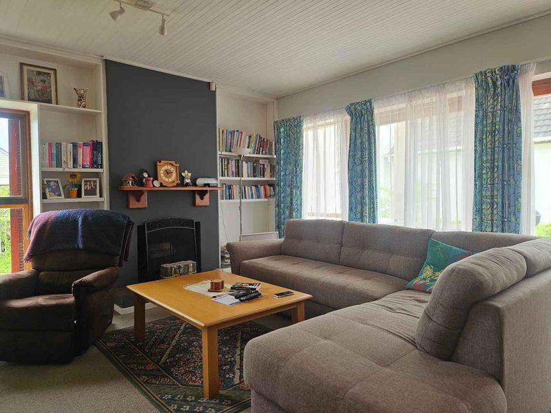 A comfortable living room featuring a fireplace with a mantelpiece, built-in shelving units, and large windows allowing for natural light.