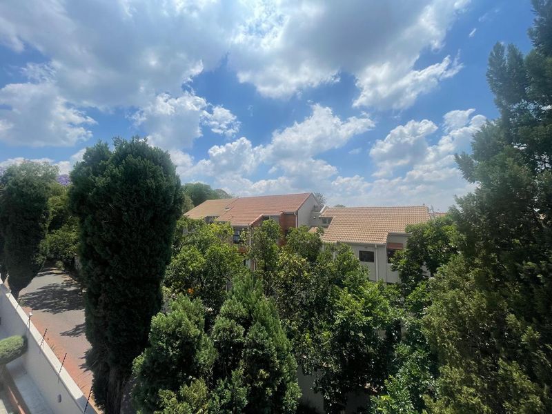 An elevated view overlooking the surrounding residential complex, featuring mature trees, tiled roof architecture, and a paved driveway area.