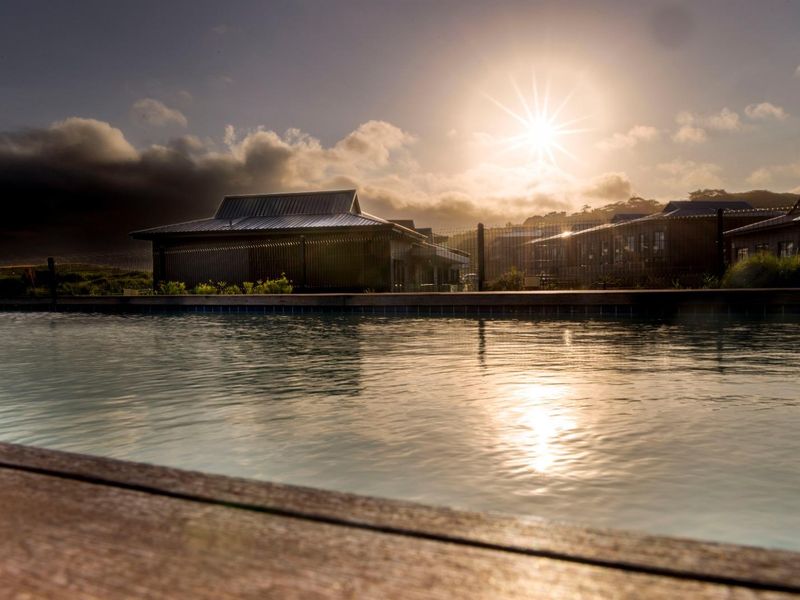 A serene outdoor swimming pool area featuring timber decking and perimeter fencing, captured during a scenic sunset.