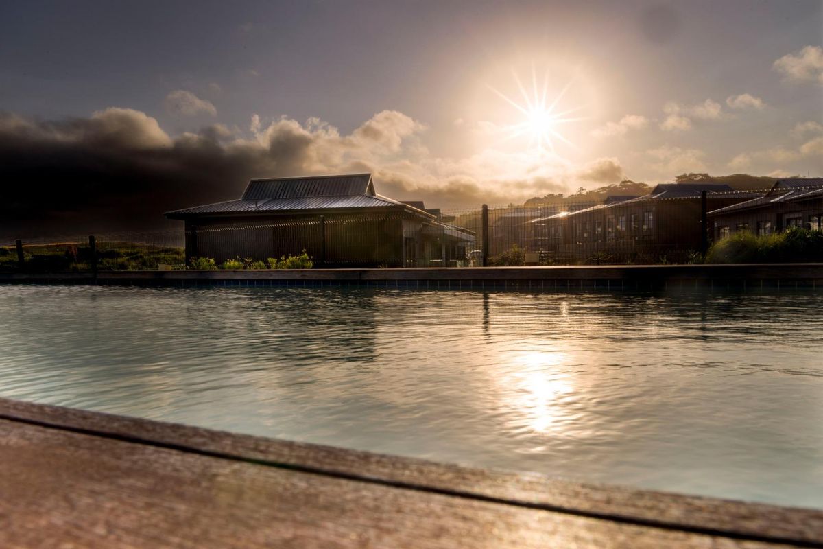 A serene outdoor swimming pool area featuring timber decking and perimeter fencing, captured during a scenic sunset.