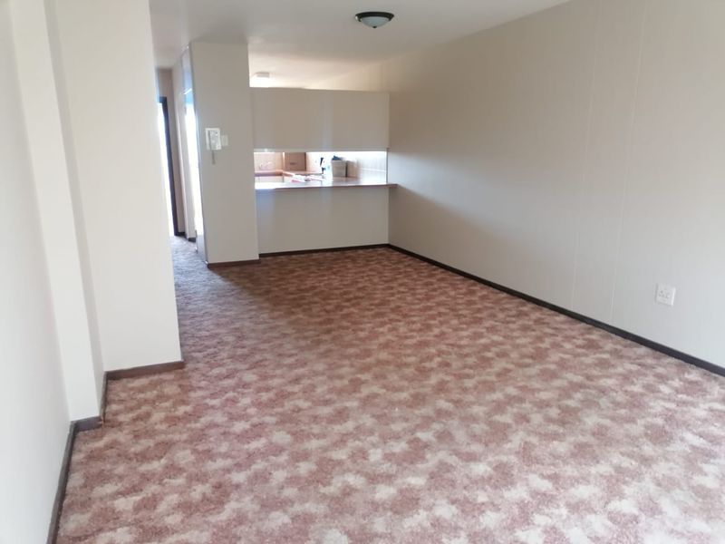 An empty open-plan living area featuring dated patterned carpet flooring and a convenient kitchen pass-through, offering a blank canvas for renovation.