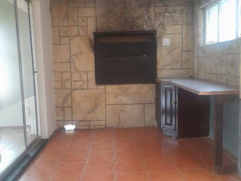Covered patio area featuring a built-in braai, stone-clad feature wall, terracotta tiling, and sliding glass doors leading to the exterior.