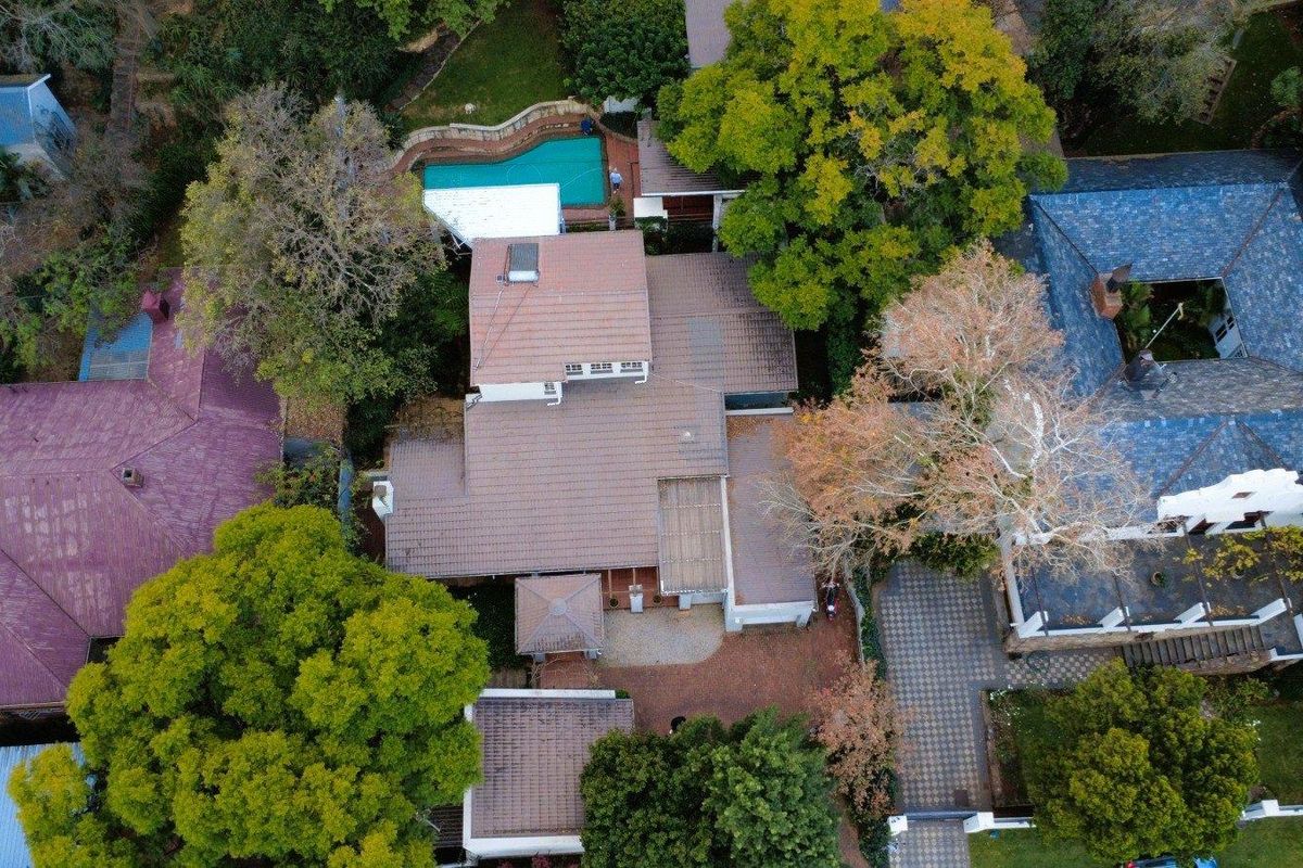 Aerial view of a residential property featuring a tiled roof house, swimming pool, paved driveway, and established garden surroundings.