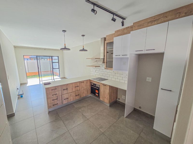 Modern open-plan kitchen featuring wood-look cabinetry, subway tile backsplash, and integrated appliances, flowing seamlessly into a bright living area with sliding door access.