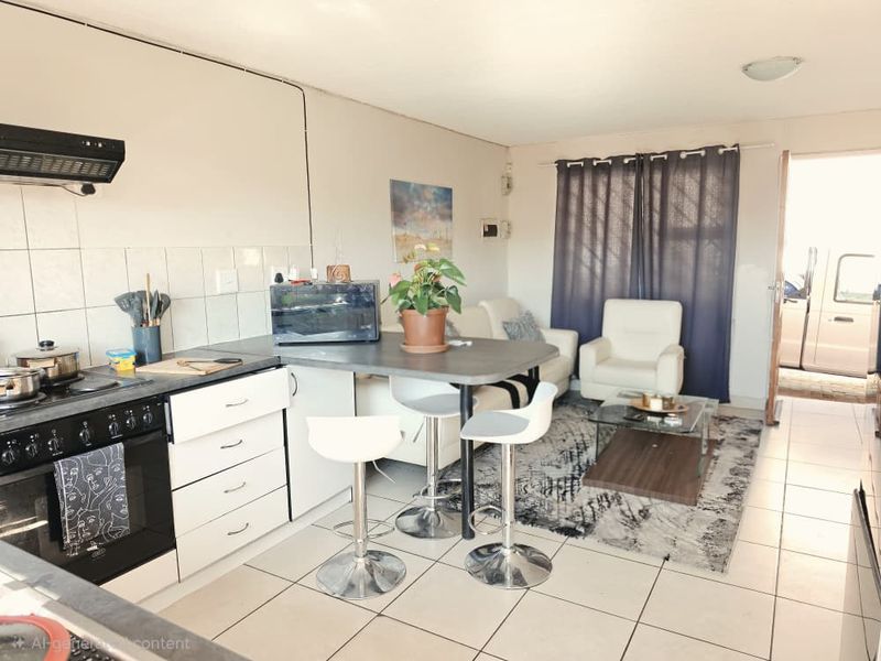 Open-plan living area featuring a functional kitchen with built-in oven, extractor fan, and tiled flooring, seamlessly connecting to the lounge space.
