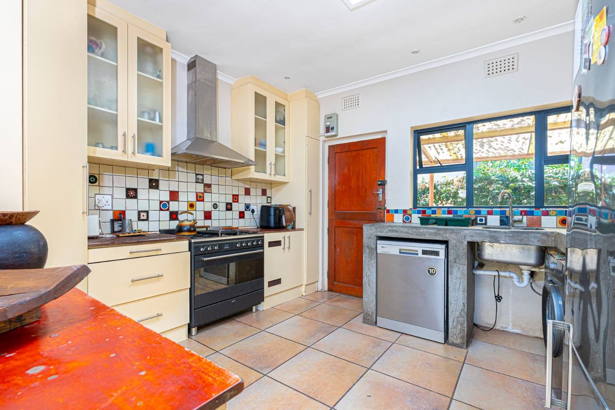 Kitchen featuring cream cabinetry, a stainless steel extractor fan, a gas stove, and a unique concrete-encased sink area with tiled splashbacks.
