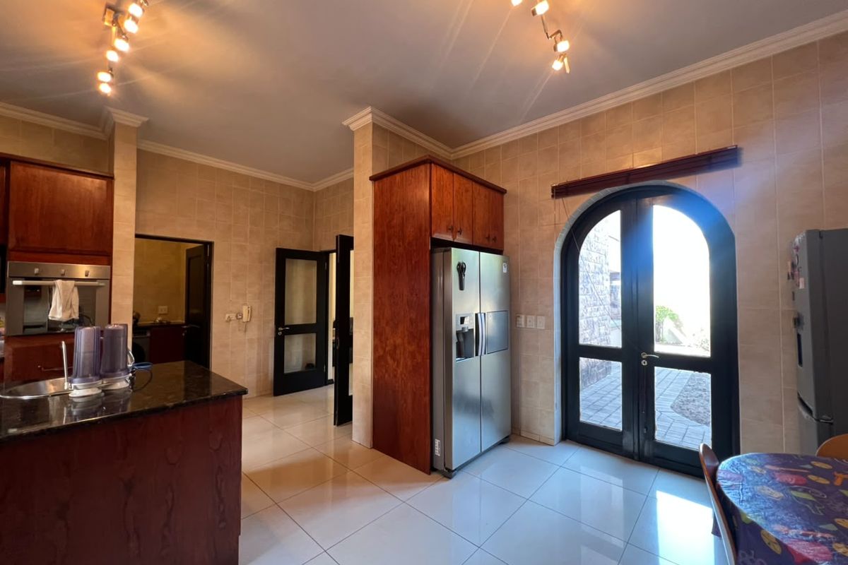 A spacious kitchen featuring dark wood cabinetry, granite countertops, tiled finishes, and an arched glass door providing direct access to the exterior.