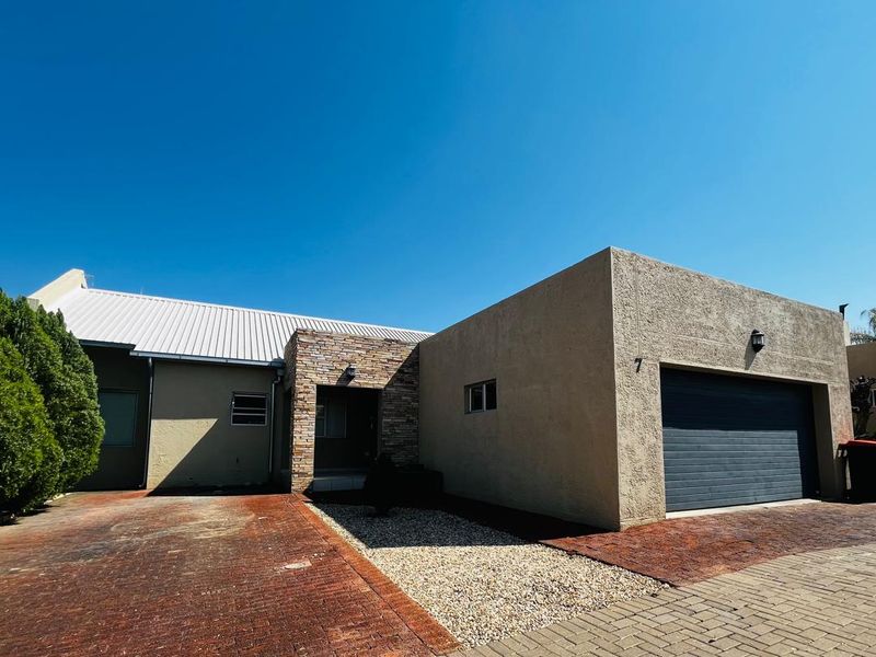 Front elevation of a townhouse featuring a stone-clad entrance, metal roof, automated garage, and brick-paved driveway with gravel landscaping.