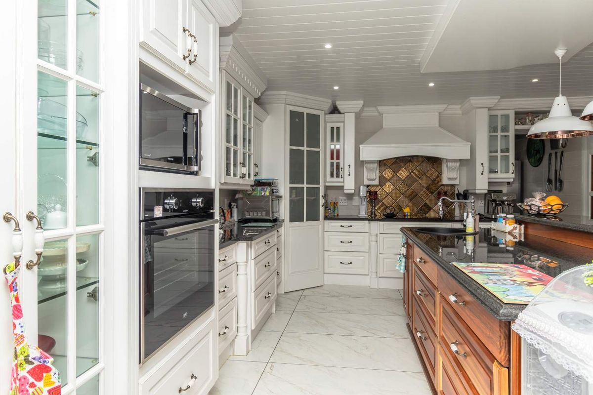 A well-appointed kitchen featuring white cabinetry, granite countertops, a central island, built-in appliances, and elegant tiled flooring.