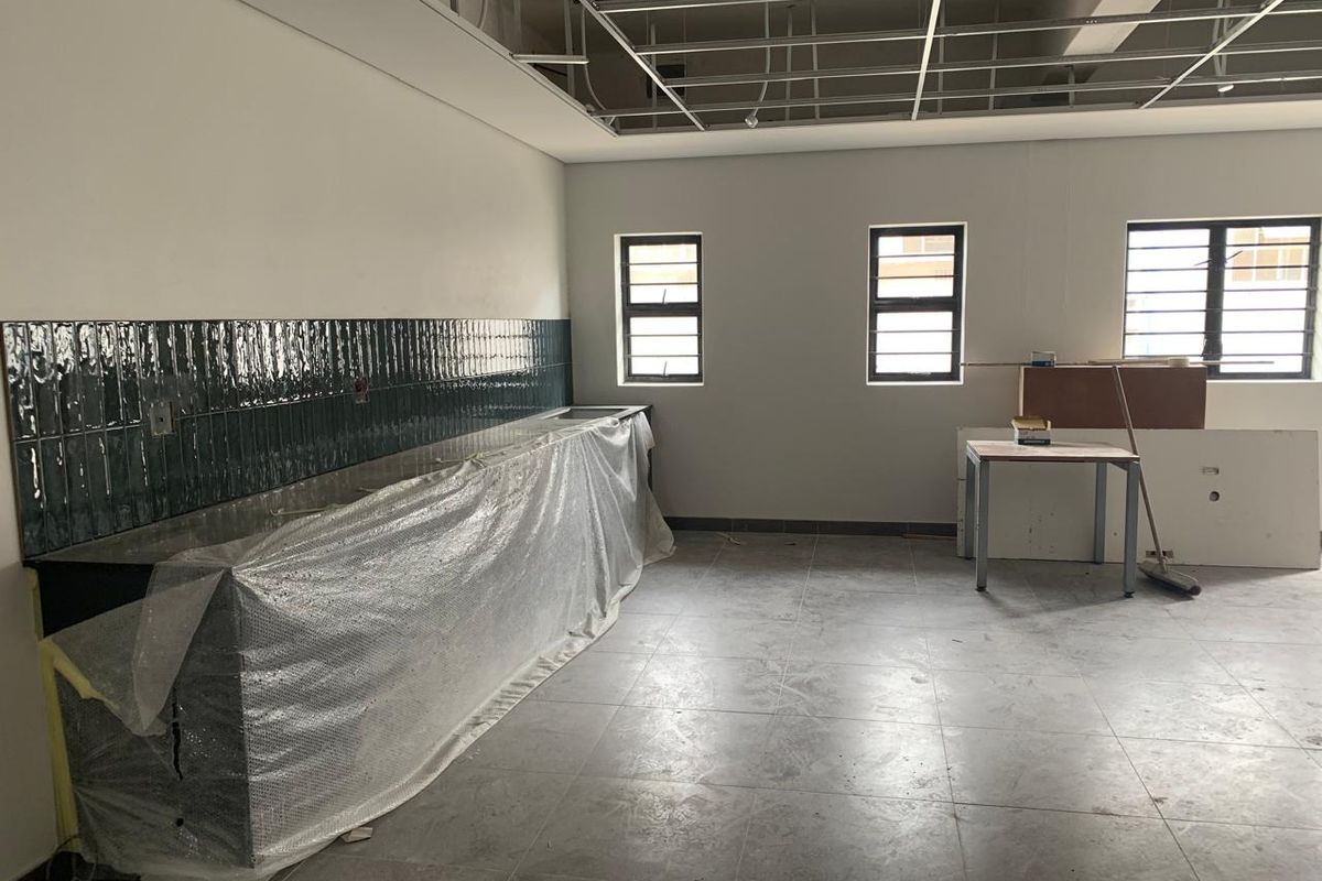 An industrial kitchen space under renovation featuring tiled splashbacks, tiled flooring, and an exposed ceiling grid ready for final installation.