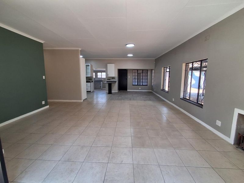 Spacious open-plan living and kitchen area featuring neutral tiled flooring, modern accent walls, and integrated kitchen cabinetry with a breakfast bar.