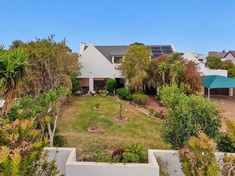 Rear view of the property featuring a well-maintained garden, paved driveway, carport, and roof-mounted solar panels.
