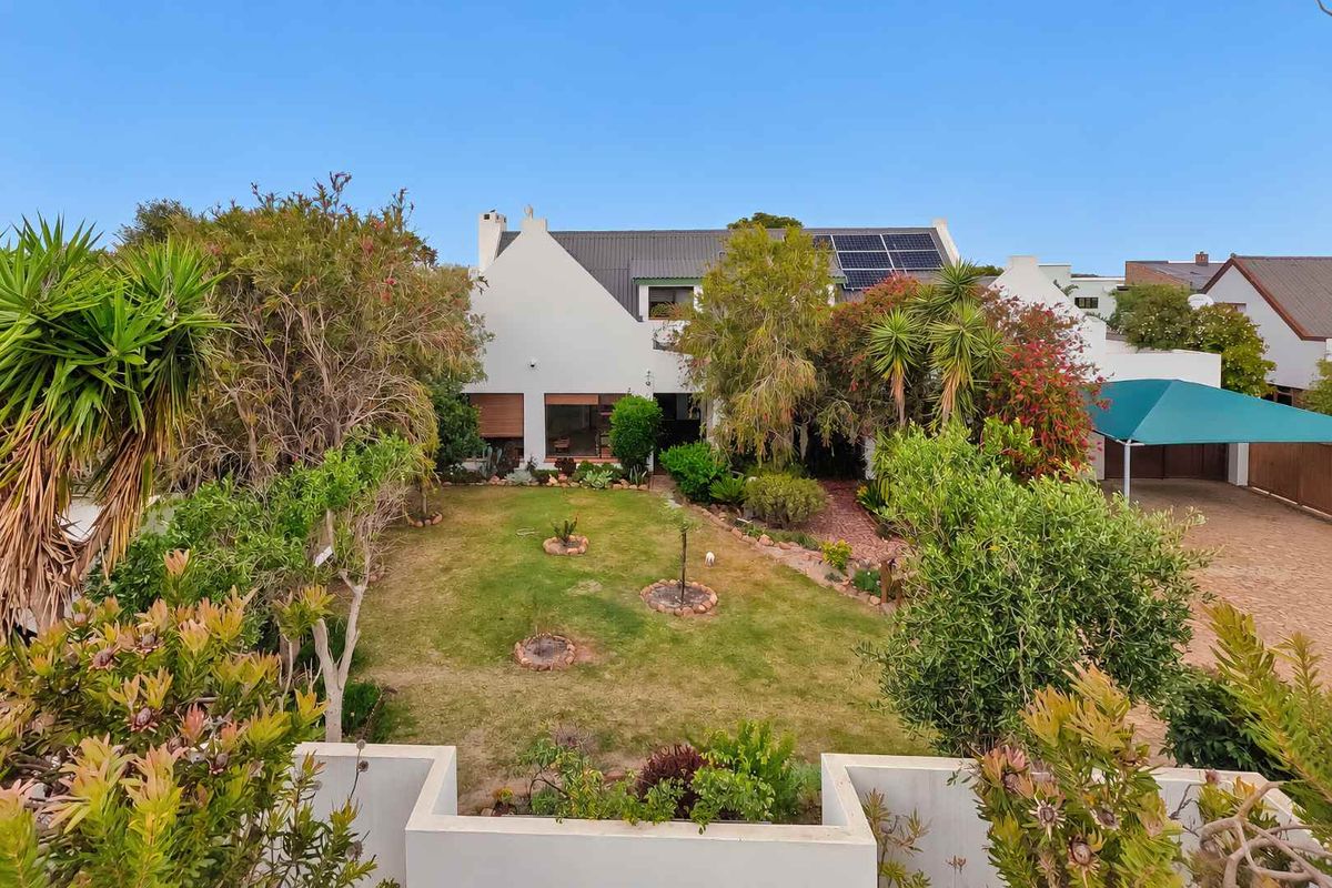 Rear view of the property featuring a well-maintained garden, paved driveway, carport, and roof-mounted solar panels.
