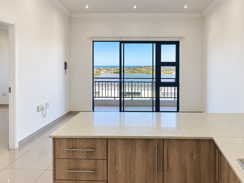Modern open-plan kitchen area featuring stone countertops, wood-finish cabinetry, and large sliding doors leading to a balcony with scenic coastal views.