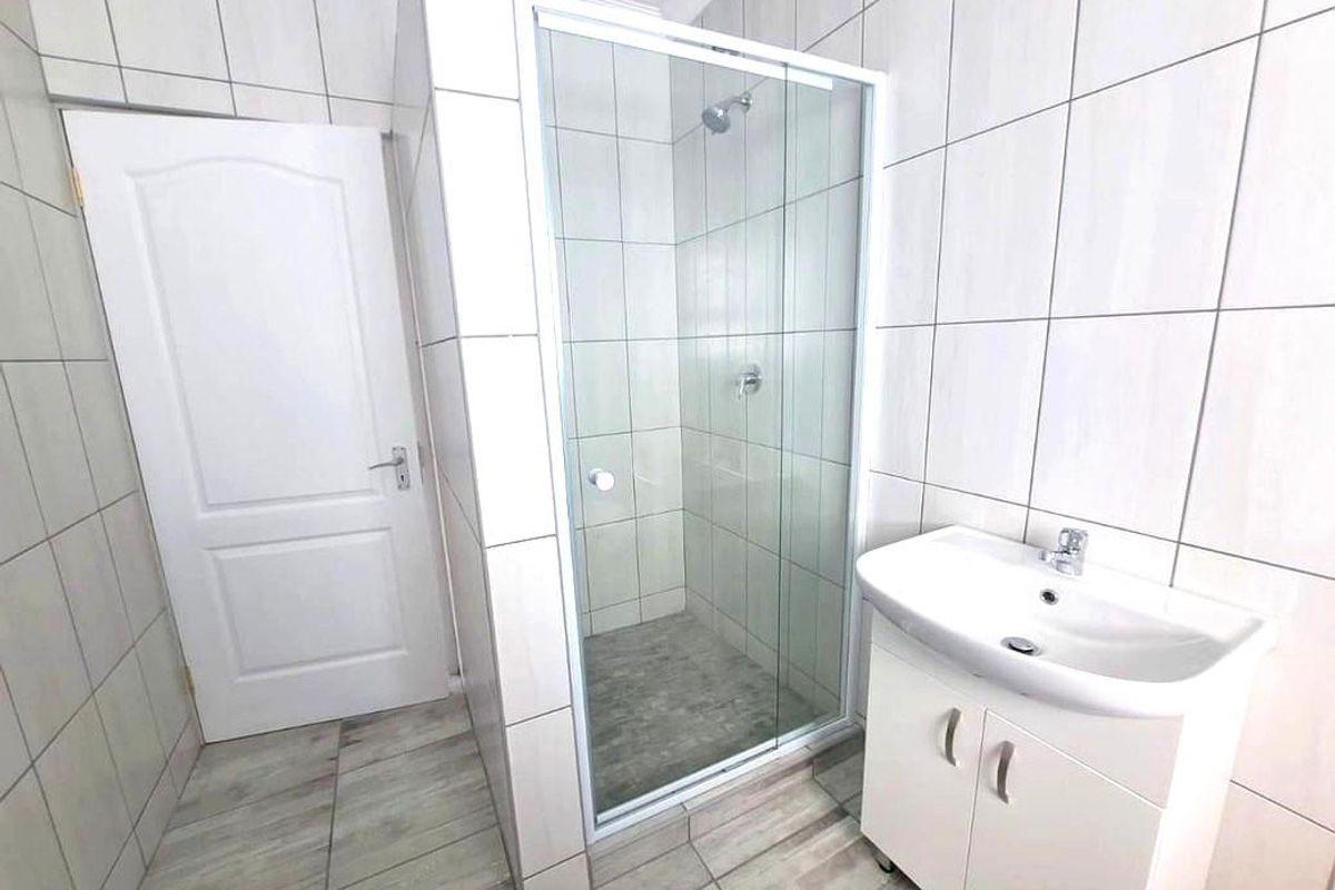 A clean, modern bathroom featuring a glass-enclosed shower, a white vanity cabinet with a basin, and neutral floor-to-ceiling wall tiles.