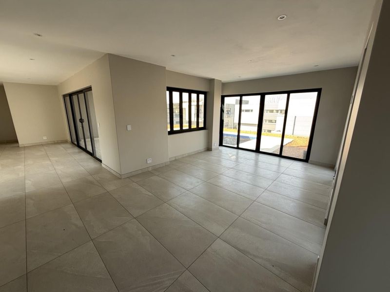 Spacious open-plan living area featuring large format floor tiles, modern black aluminium sliding doors, and abundant natural light with a view of the pool.