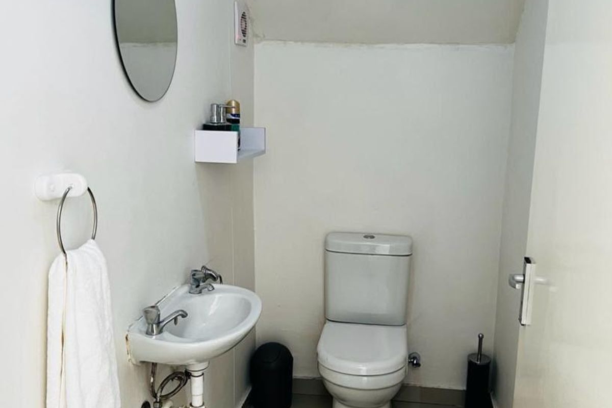 A compact guest bathroom featuring a wall-mounted basin and a standard toilet with neutral floor tiling.