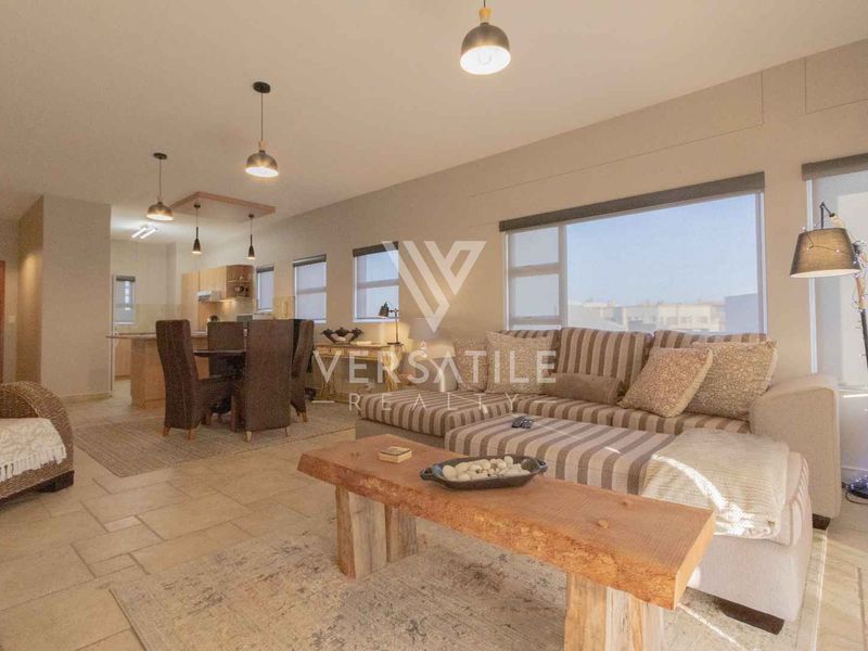 Spacious open-plan living and dining area featuring tiled flooring, modern pendant lighting, and a functional kitchen with an island, all bathed in natural light.