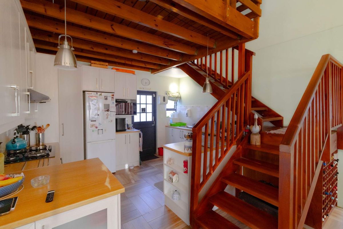 A functional kitchen featuring white cabinetry, timber staircase, and exposed ceiling beams, creating a warm and open-plan atmosphere.