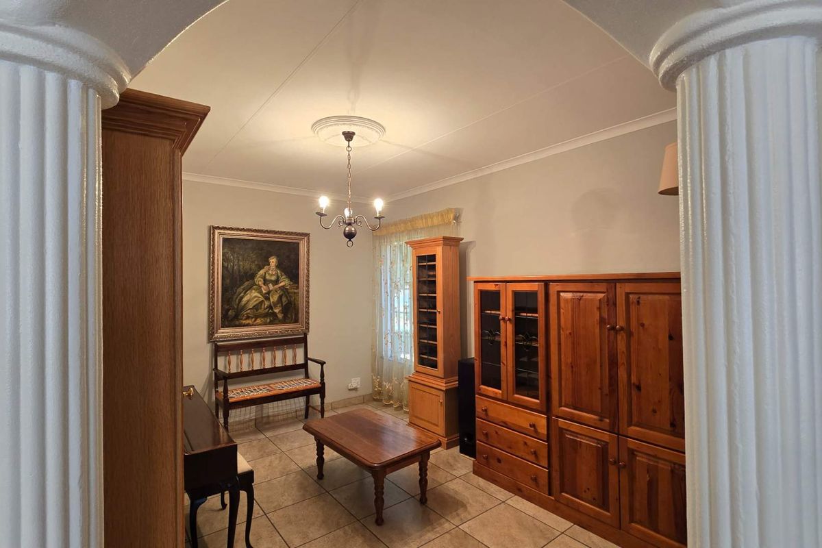 A living area featuring tiled flooring, a decorative ceiling rose, and classic architectural columns framing the entrance.