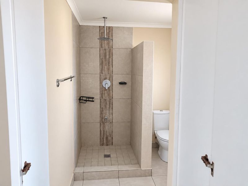 A clean, modern bathroom featuring a walk-in shower with a rainfall shower head, neutral wall tiles, and a standard toilet.