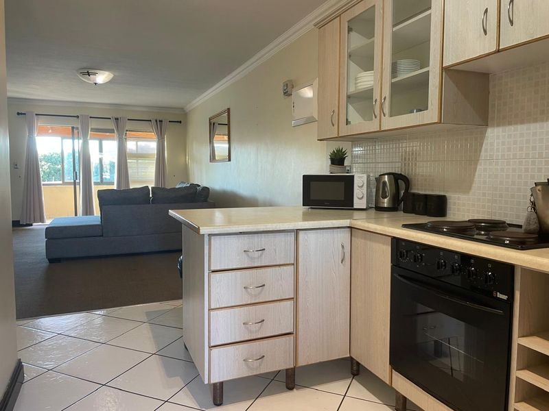 Open-plan living area featuring a functional kitchen with built-in cabinetry and appliances, flowing into a spacious lounge with access to a balcony.