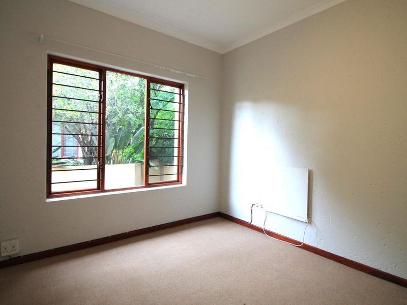 A vacant bedroom featuring carpeted flooring, timber-framed windows with security bars, and a wall-mounted heater.