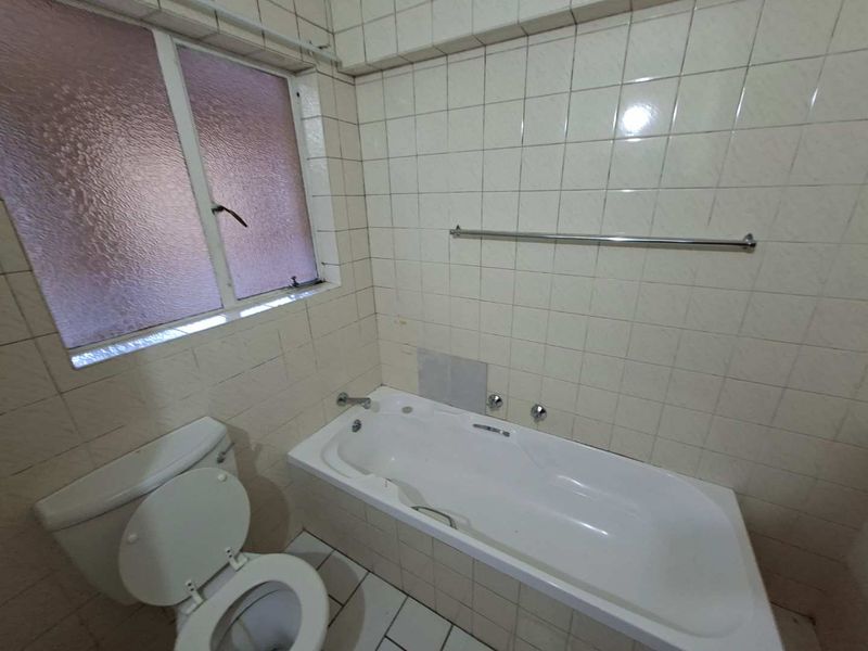 A dated bathroom featuring a built-in bathtub, toilet, and tiled finishes, offering potential for modernization and renovation.