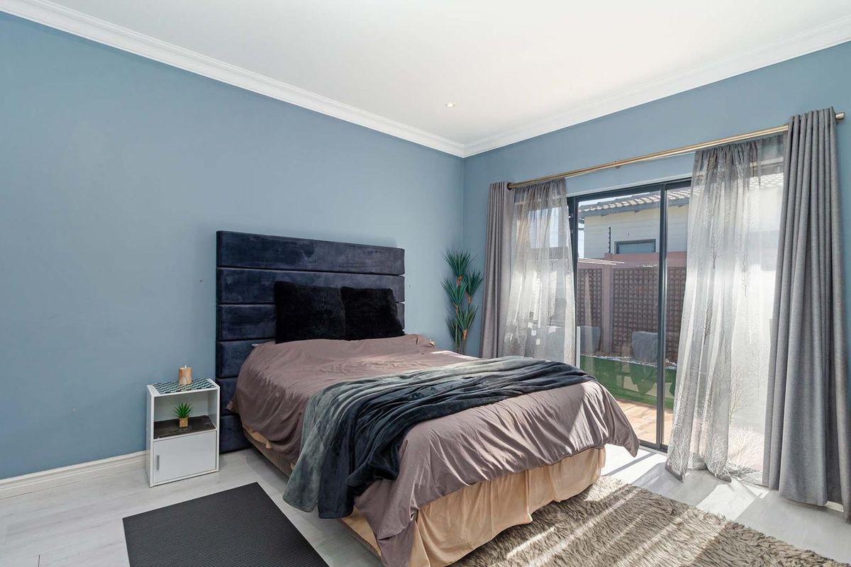 A well-maintained bedroom featuring light-toned laminate flooring, cove cornicing, and a sliding glass door providing direct access to the rear garden area.