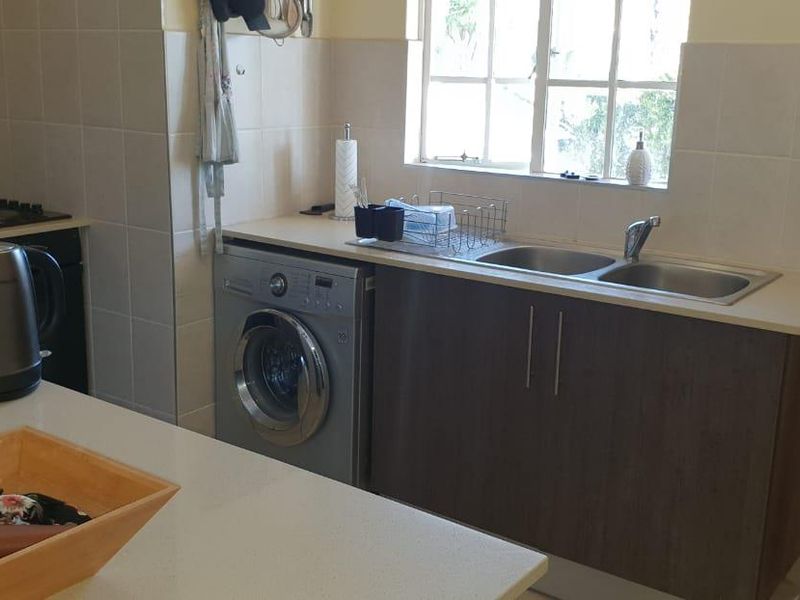 A functional kitchen area featuring built-in cabinetry, a double sink, tiled backsplash, and space for an integrated washing machine.