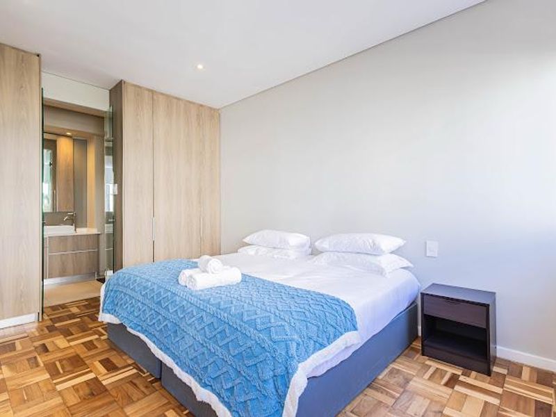 Modern bedroom featuring high-quality parquet flooring, ample built-in cupboard storage, and direct access to an en-suite bathroom.
