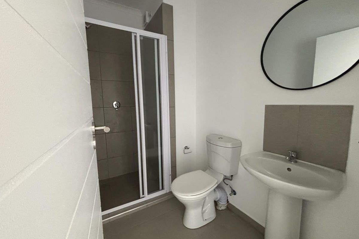 A clean, functional bathroom featuring a walk-in shower with tiled surround, a pedestal basin, and a standard toilet.