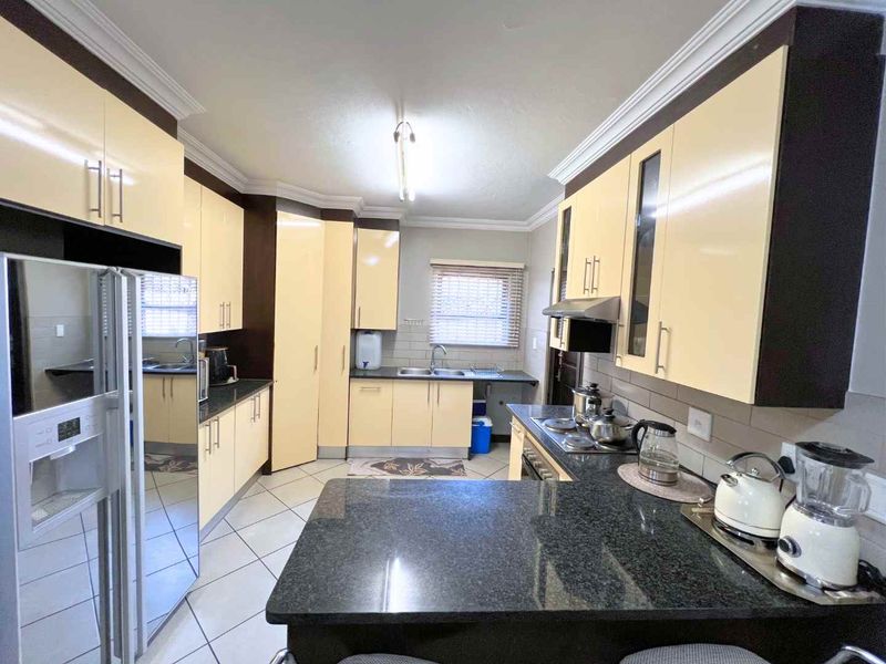 A functional kitchen featuring granite countertops, ample built-in cabinetry, a double basin sink, and tiled flooring with a classic layout.