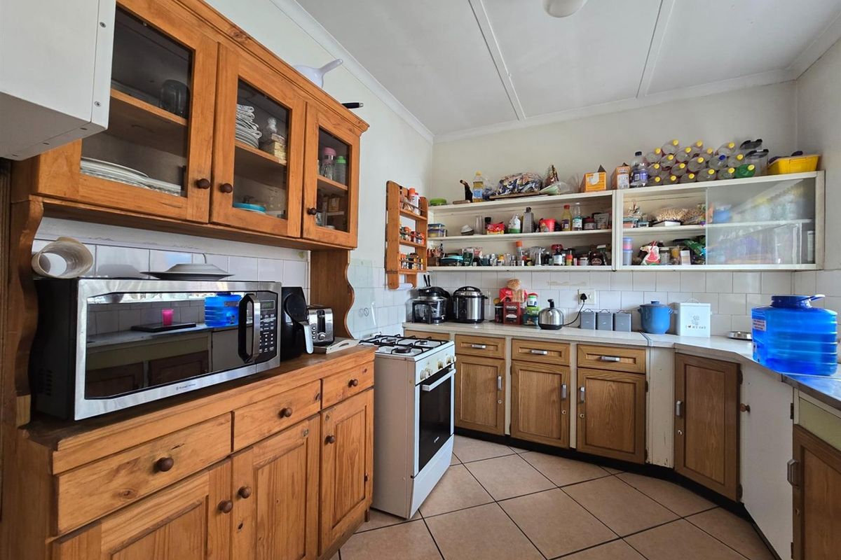 A functional kitchen featuring traditional wooden cabinetry, tiled flooring, a gas stove, and ample built-in shelving for storage.