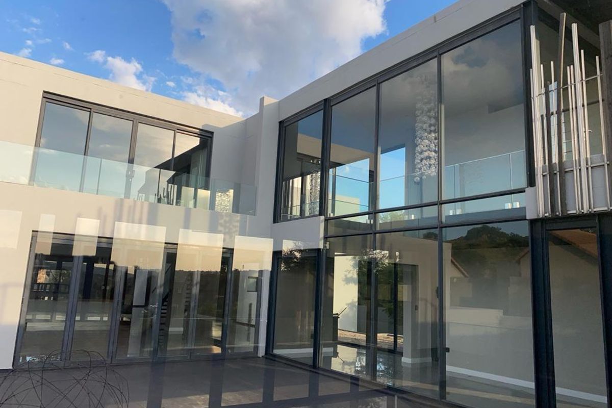 Modern double-story rear facade featuring extensive floor-to-ceiling glass, sleek architectural lines, and a spacious tiled patio area.