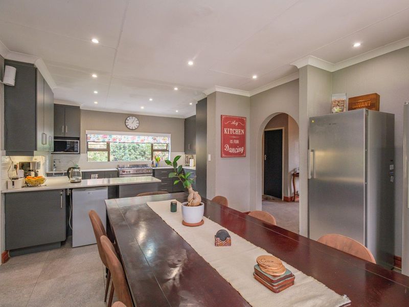 An open-plan kitchen and dining area featuring modern grey cabinetry, stone countertops, a gas stove, and recessed lighting, connected by an elegant archway.