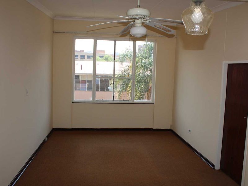 An empty bedroom featuring carpet flooring, a ceiling fan, and a large window providing natural light.