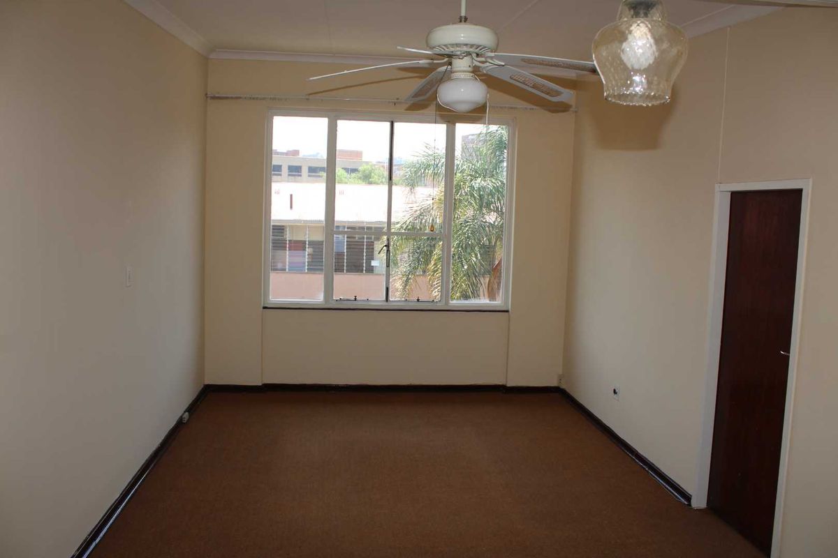 An empty bedroom featuring carpet flooring, a ceiling fan, and a large window providing natural light.